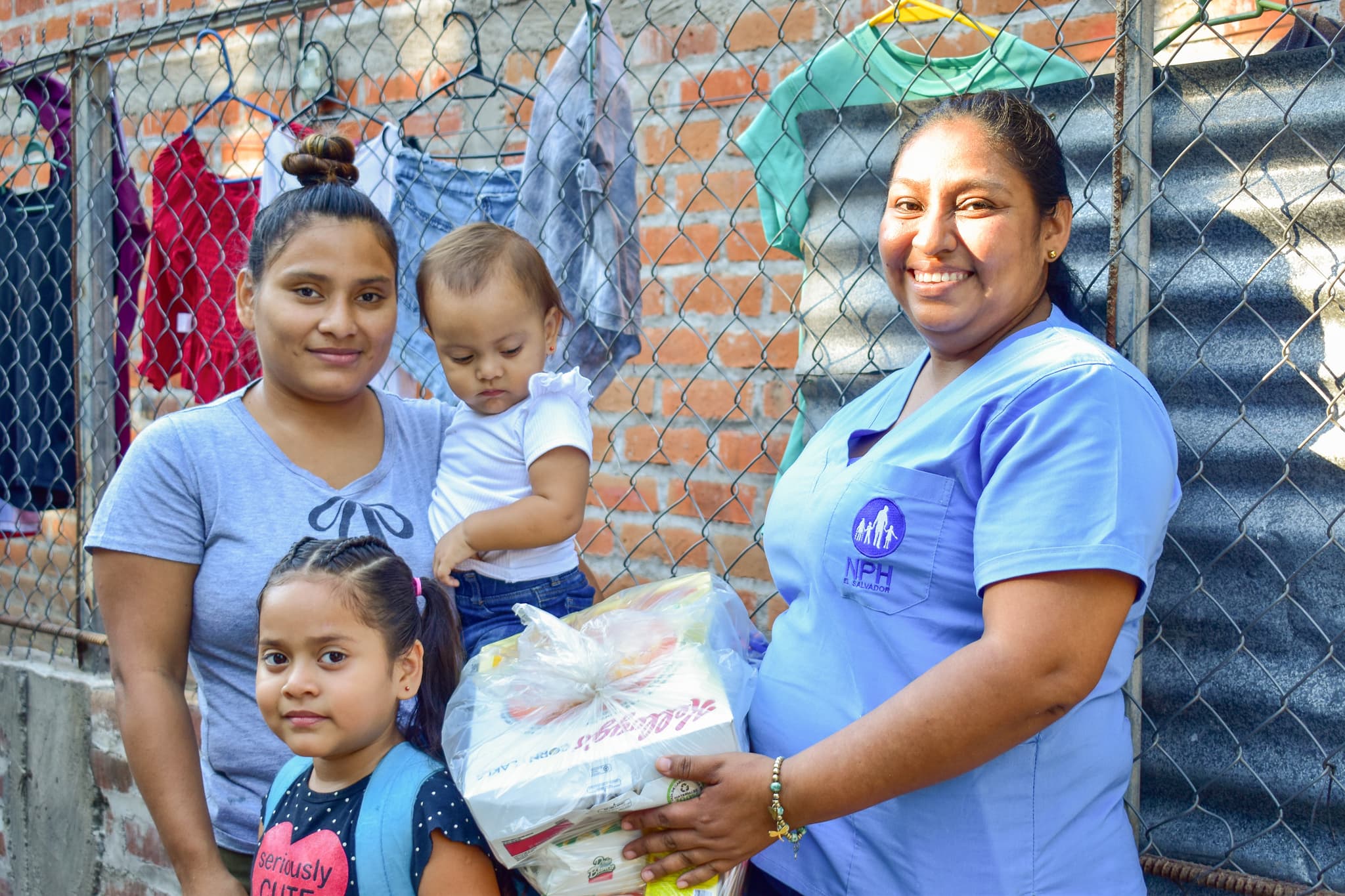 Eine Familie aus El Salvador steht vor einem Zaun mit einer nph Mitarbeiterin